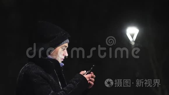 街灯里的那个人。 那家伙看着他的智能手机。 在灯的背景下下雪。 慢动作