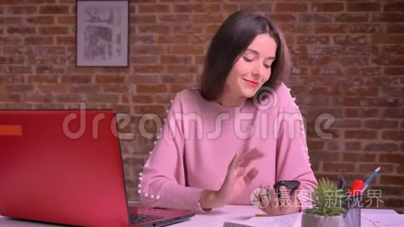快乐的年轻女性在工作场所用红色笔记本电脑在砖背景前刷卡