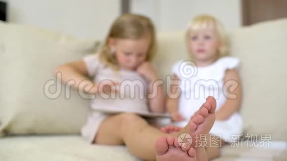 两个孩子在家用平板电脑看ang。 儿童使用现代笔记本电脑，平板电脑在沙发上。 小女孩在玩