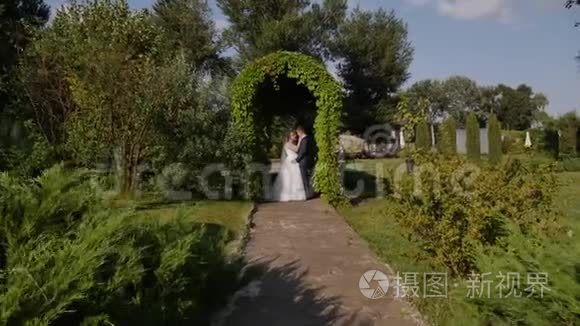 高清特写拍摄的新婚夫妇在公园的绿色弧线中拥抱亲吻