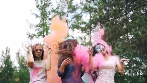 当人们向她们投掷五颜六色的面粉时，快乐的年轻女士在粉末涂料的云中翩翩起舞