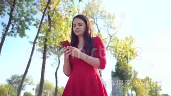 漂亮的商务女性穿着红色连衣裙在城里散步，并在智能手机上使用应用程序