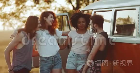 四个多元文化的好朋友在他们的橙色面包车旁的场地中间度过了愉快的时光，每个人都拿着