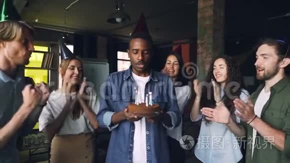 兴奋的非洲裔美国人在生日蛋糕上吹蜡烛，在他的团队中大笑