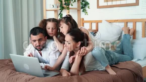 家庭幸福，父母和两个女儿在笔记本电脑上看卡通，慢动作视频的预览图