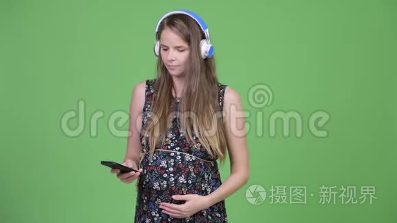 年轻快乐的孕妇一边听音乐一边用电话