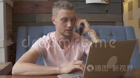 英俊的商人在电话里说话，在笔记本电脑上工作时微笑。