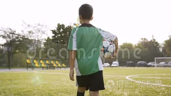 小男孩手里拿着足球走路。