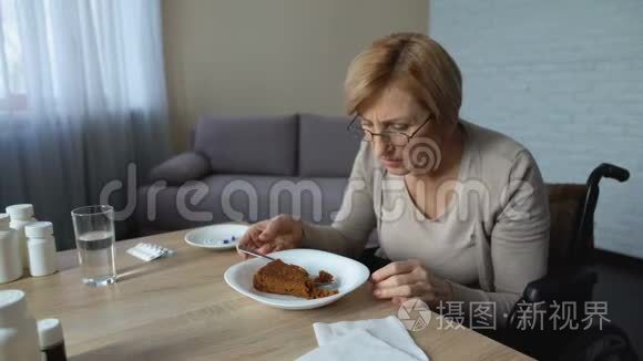 孤独的老奶奶坐在轮椅上慢慢地在桌旁吃着午饭