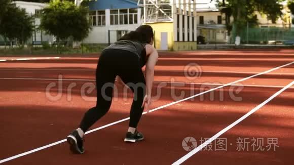一个女跑步者开始在小型户外体育场的跑道上跑步的慢动作镜头。 适合的女孩