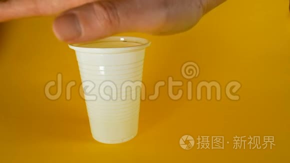 一个男人`他的手在黄色的背景上捏碎一个白色的一次性塑料杯，这是生态和其他主题的理想素材