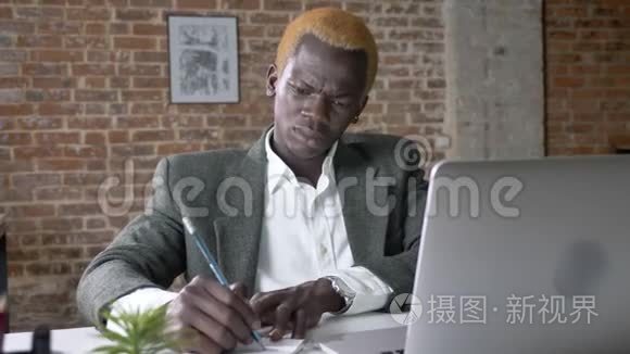 年轻严肃的非裔美国商人从笔记本电脑上写笔记，坐在现代办公室里，集中精力，