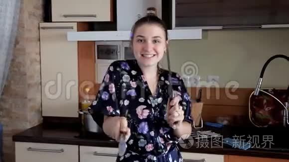一个年轻的女孩在厨房里打扫卫生，开玩笑跳舞。 早上好心情