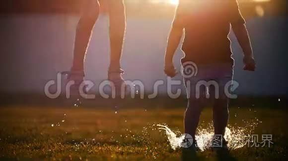 女孩和男孩在草地上的水坑上跳跃。 在阳光下闪闪发光的飞行喷雾。
