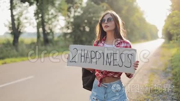 年轻美女搭便车站在路上举着2个幸福的标志。 夏季