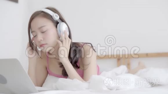 美丽的年轻亚洲女人躺在卧室里用手提电脑放松听音乐，女孩在家里看视频聊天