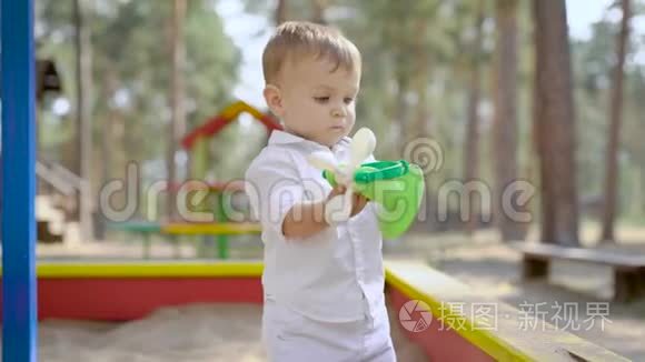 有趣的小男孩夏天站在公园的沙箱里独自玩塑料玩具