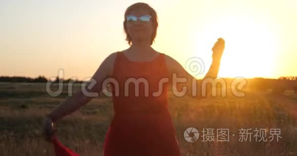 在夕阳下，穿着红色裙子在大片田野里跳舞的时髦女人微笑着