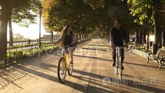 夏季在城市公园或林荫大道上骑自行车的年轻快乐夫妇或朋友的正面景色。 人民