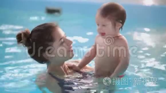 可爱的小宝宝和他妈妈在游泳池里上游泳课。 妈妈把儿子抱在手里，