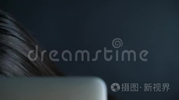 年轻女子戴着眼镜，眼睛盯着显示器后面，眼睛里闪着光