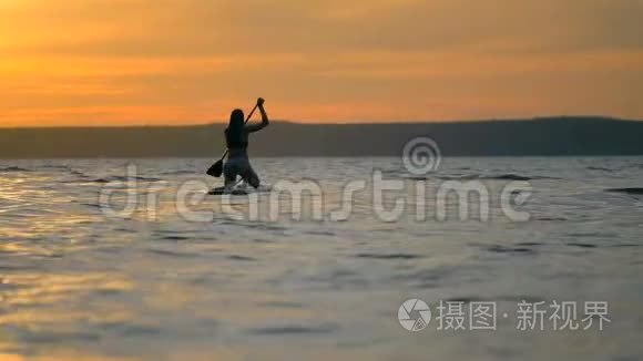 冲浪女孩漂浮在冲浪板上，景色宜人。 女人在水中冲浪时拉桨。