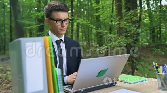 快乐的年轻商人完成他的工作，在绿色森林的椅子上放松