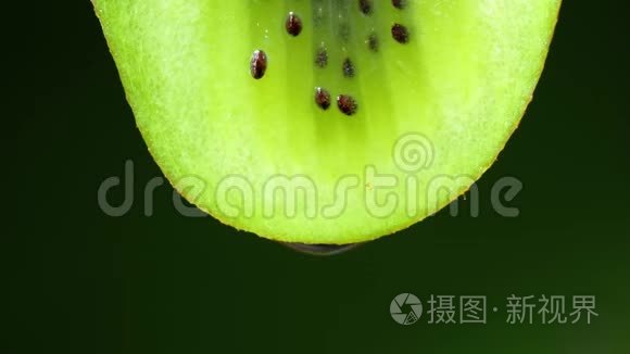 一片猕猴桃的近缘或宏观，一滴水缓慢地落下。 黑色背景