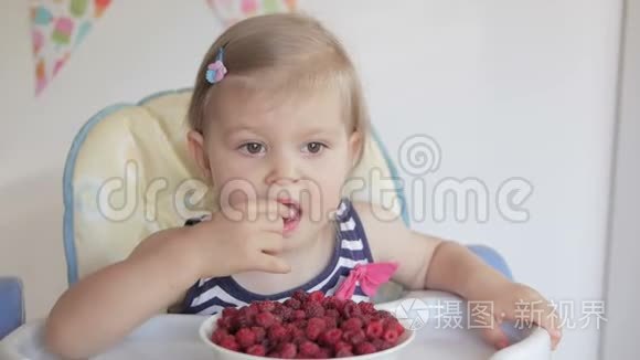 一个小女孩坐在孩子们`桌子旁吃成熟的红树莓