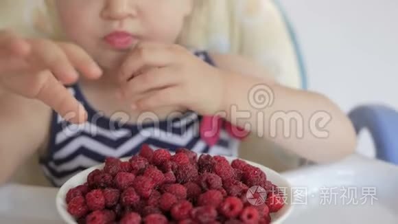 一个小女孩坐在孩子们`桌子旁吃成熟的红树莓