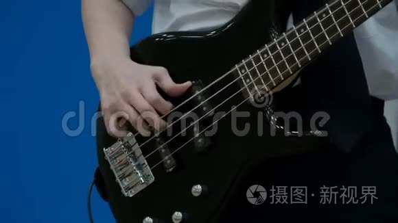 男青少年低音吉他手演奏黑色电吉他。 特写镜头。 一个少年的手指在用低音吉他拉弦.