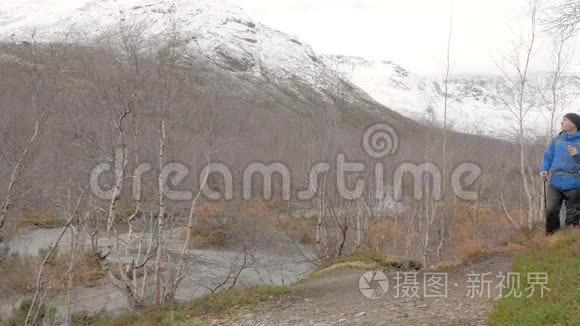 一个中年男人带着背包旅行一条山路。 他停下来，看着山顶，继续往前走。