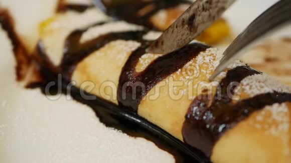 顾客用叉子和刀子吃美味的薄饼卷，上面放着新鲜芒果、巧克力和糖粉视频的预览图
