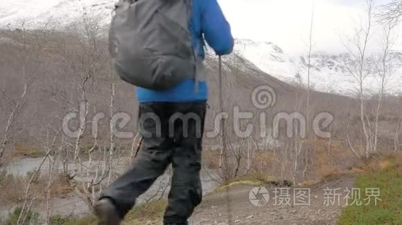 一个中年男人带着背包旅行一条山路。 他停下来，看着山顶，继续往前走。