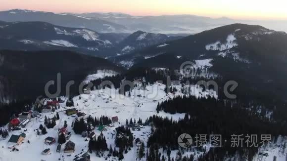 华丽的空中拍摄，山上覆盖着树木和雪，前面有一个小村庄，4k