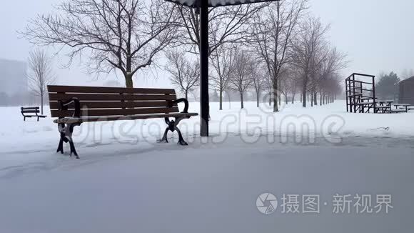 白天与公园长凳的雪景。 白雪皑皑的风景，公共公园的建筑笼罩着乌云