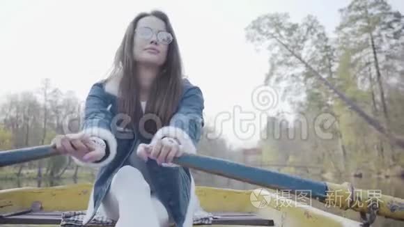 一位戴眼镜的迷人年轻女子和一件牛仔夹克漂浮在湖面或河流上的船上的肖像。 美丽美丽