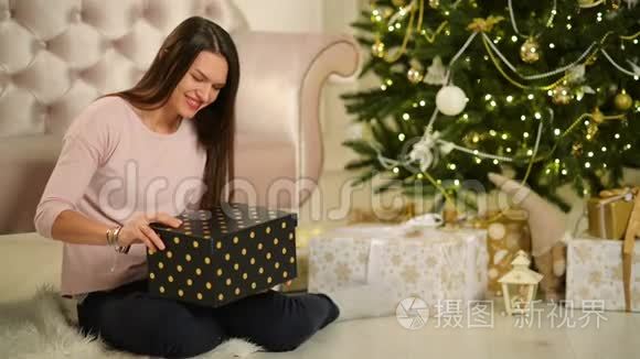 美丽的幸福女人坐在圣诞树旁边，手里拿着礼物。 圣诞快乐，新年理念。
