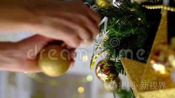 女人`手用金色玩具装饰圣诞树. 背景上的仙女灯。