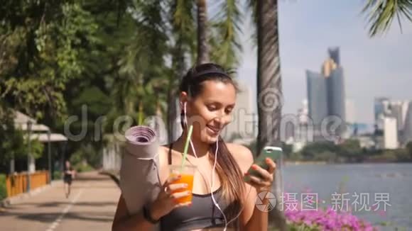 美丽的适合混合种族妇女使用手机应用程序和饮用新鲜橙汁后，上午瑜伽练习。