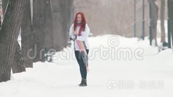 冬季公园。 一个开朗的女人，一头鲜红的头发站在人行道上，做一个雪球，朝前扔去