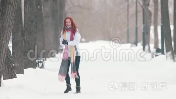 冬季公园。一个留着鲜红头发的女人站在人行道上，做一个雪球，然后把它向前扔