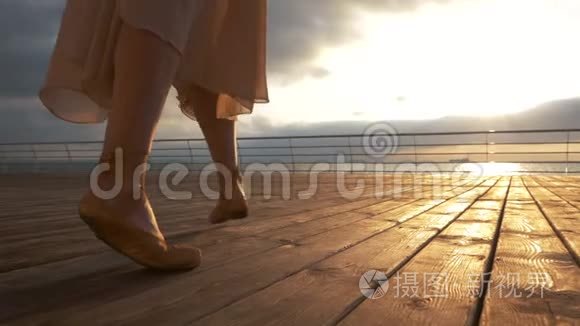 穿着米色丝绸连衣裙的年轻芭蕾舞女在木堤上穿着尖鞋跑向大海或海洋。 日出背景