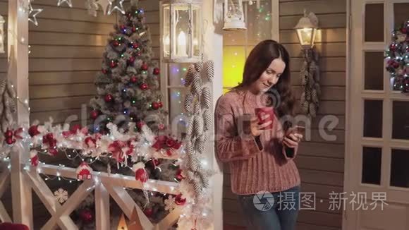 女人微笑着喝茶，在门廊用电话，背景是圣诞树