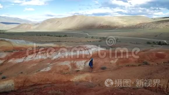 年轻的旅游妇女带着背包和帽子爬上红石山。 那里风景不真实，多云