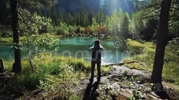 一位年轻的女游客正站在一个美丽的蓝色湖泊上，在阳光明媚的日子里，为风景优美的风景拍照