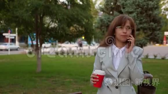 女商人戴着浅色西装眼镜，在公园里散步，喝咖啡，在智能手机上聊天