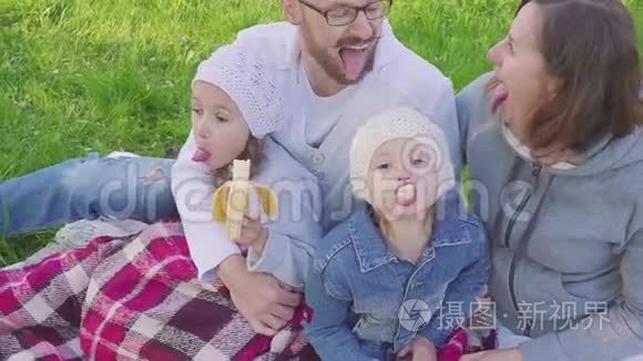 爸爸、妈妈和两个女儿在野餐时唱着歌，做着脸