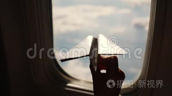 特写镜头。 一个孩子的手`小纸飞机在飞机窗口的背景下的剪影。 儿童
