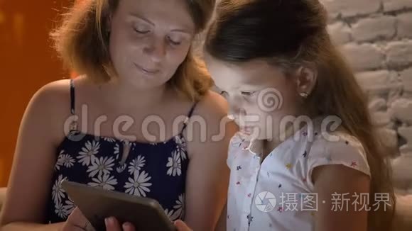 母亲带着小女儿在平板电脑上打字，坐在家里的沙发上，家庭观念在室内